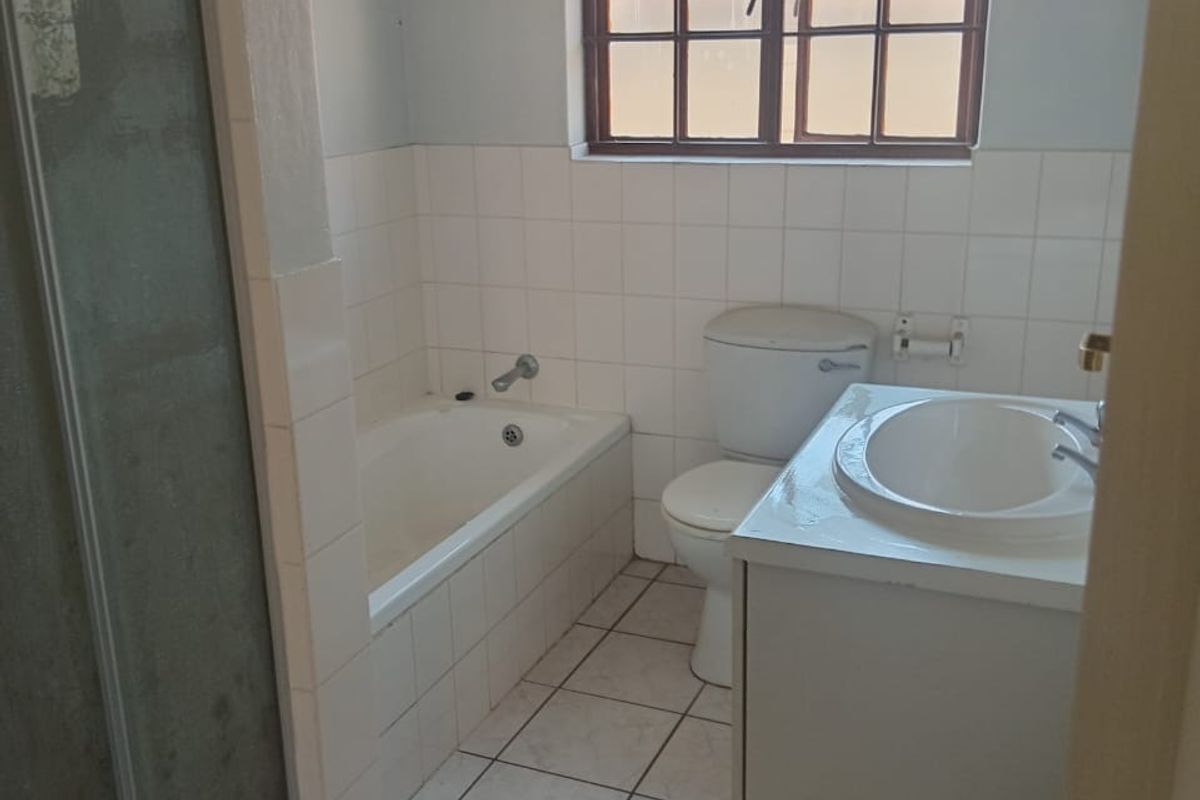 A functional bathroom featuring a built-in bathtub, separate shower enclosure, vanity cabinet with basin, and toilet, finished with tiled flooring and wall splashbacks.