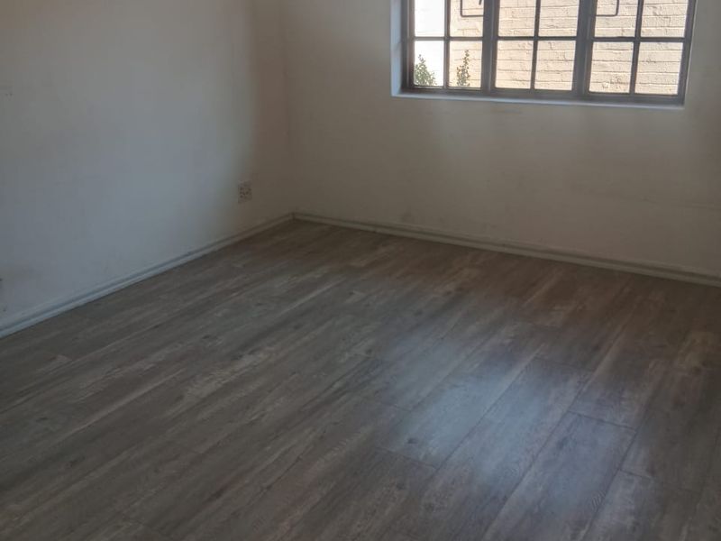 An empty bedroom featuring modern laminate flooring and a grid-pattern window, providing a neutral canvas for personalization.