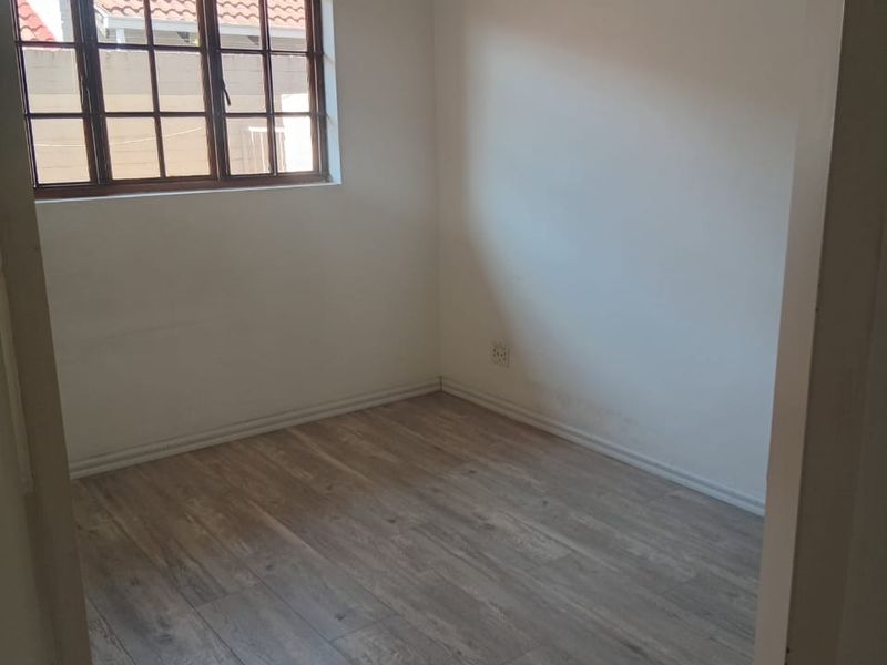 An empty bedroom featuring light-toned laminate flooring and a timber-framed window, providing a neutral canvas for interior design.