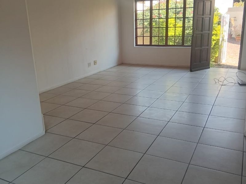 An empty, open-plan living area featuring neutral floor tiles and a warm timber-clad ceiling, with direct access to an outdoor patio area.