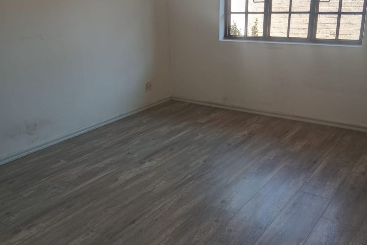 An empty bedroom featuring modern laminate flooring and a large grid-pattern window, providing a blank canvas for interior design.