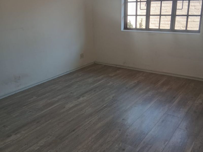 An empty bedroom featuring modern laminate flooring and a large grid-pattern window, providing a blank canvas for interior design.