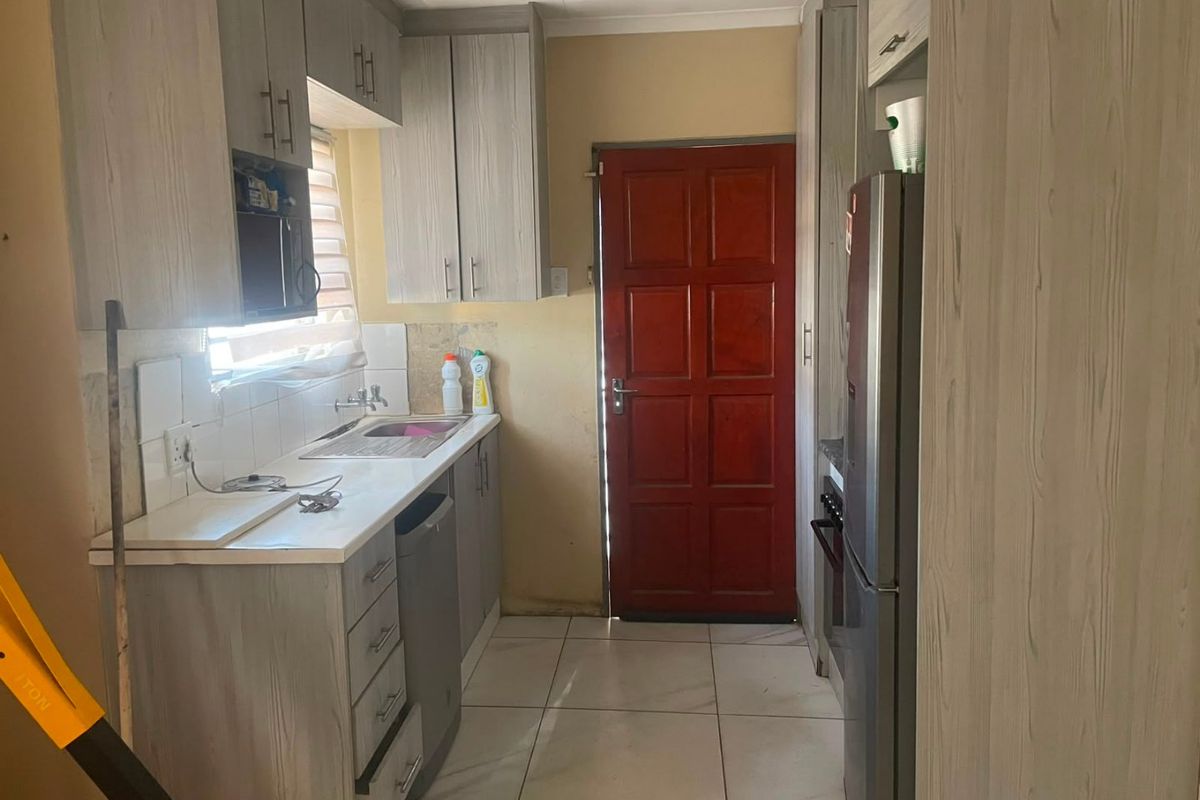 A functional kitchen featuring light wood-grain cabinetry, tiled flooring, and a tiled backsplash, providing a practical workspace with direct access to an exterior door.