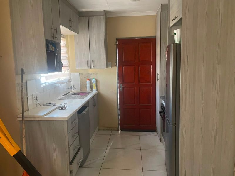 A functional kitchen featuring light wood-grain cabinetry, tiled flooring, and a tiled backsplash, providing a practical workspace with direct access to an exterior door.