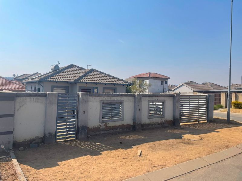 Front view of a residential property featuring a concrete perimeter wall with metal gates and a tiled roof house with a solar water heater.
