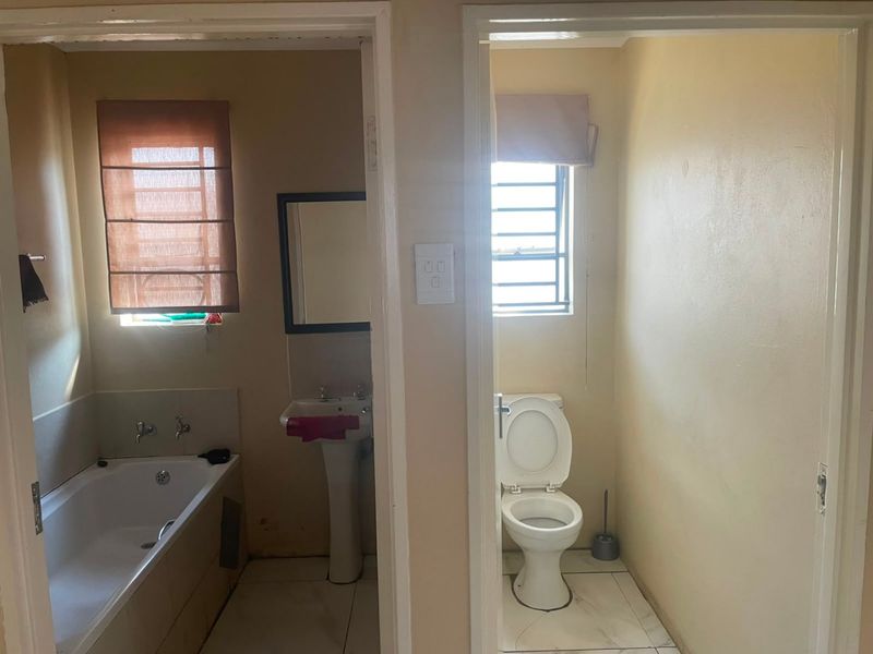 A functional bathroom layout featuring a separate bathtub and pedestal sink area adjacent to a private toilet room with tiled flooring.