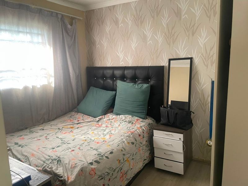 A compact bedroom featuring laminate flooring and a decorative patterned feature wall, providing a cozy and functional sleeping space.