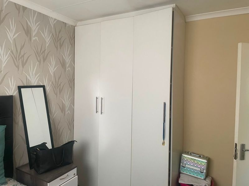 A bedroom featuring a white built-in wardrobe with modern handles, complemented by patterned wallpaper and neutral wall tones.
