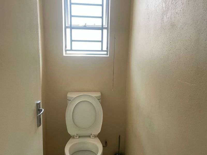 A compact, functional guest toilet featuring tiled flooring and a window with security bars.
