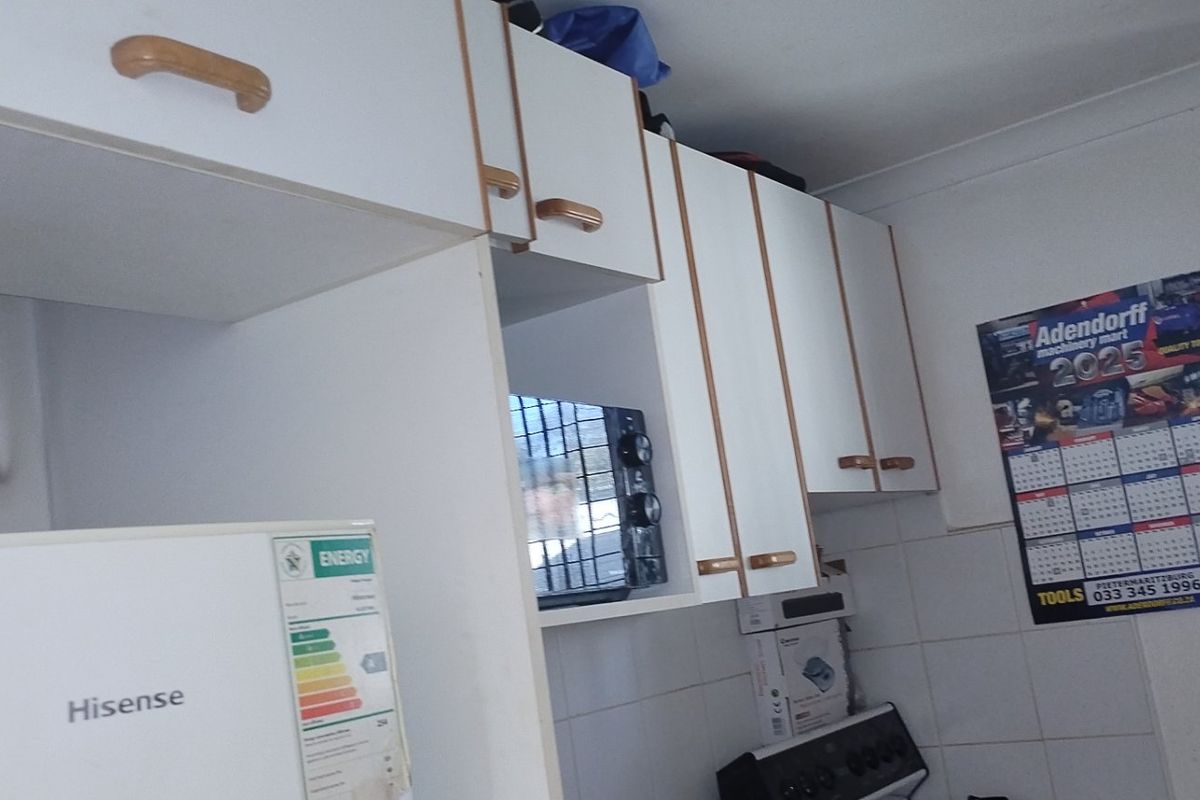 A functional kitchen area featuring white built-in cabinetry, tiled splashbacks, and space for a freestanding stove.