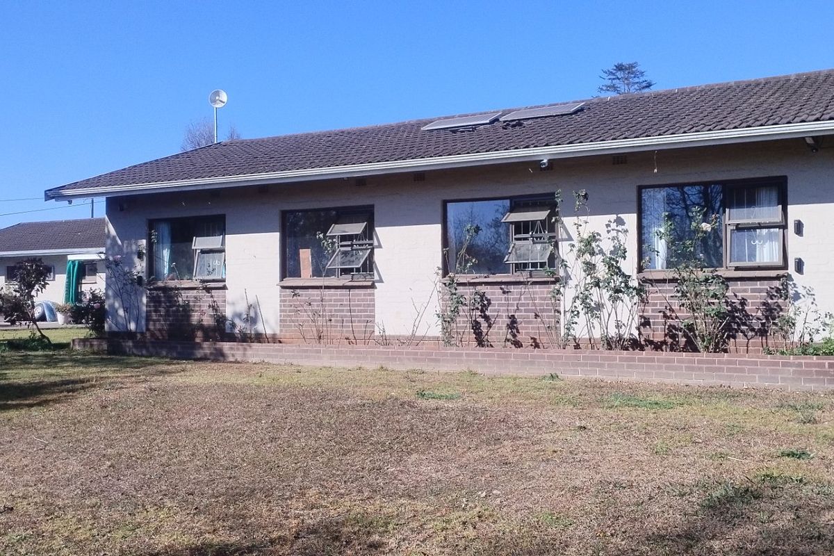 A rear view of a single-story brick house featuring a tiled roof, solar panels, and a garden with a brick planter box.