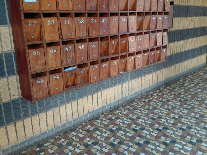 A communal apartment building entrance area featuring a large wall-mounted wooden mailbox unit and decorative mosaic tile flooring.