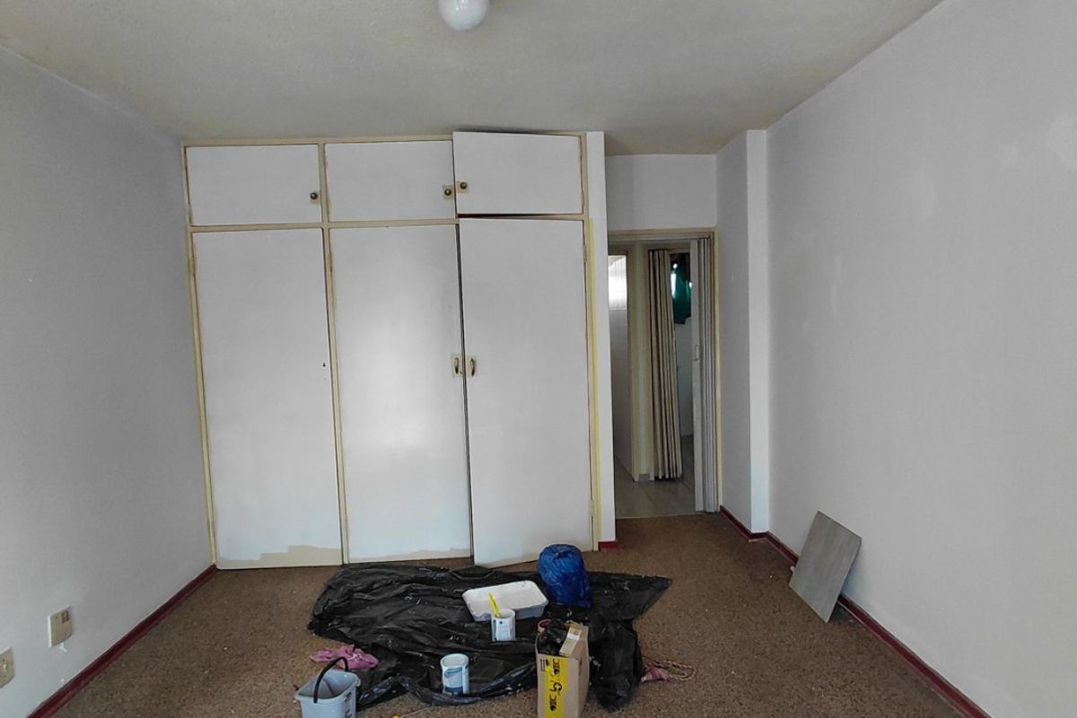 An empty bedroom featuring built-in cupboards and carpeted flooring, currently undergoing minor maintenance and painting.
