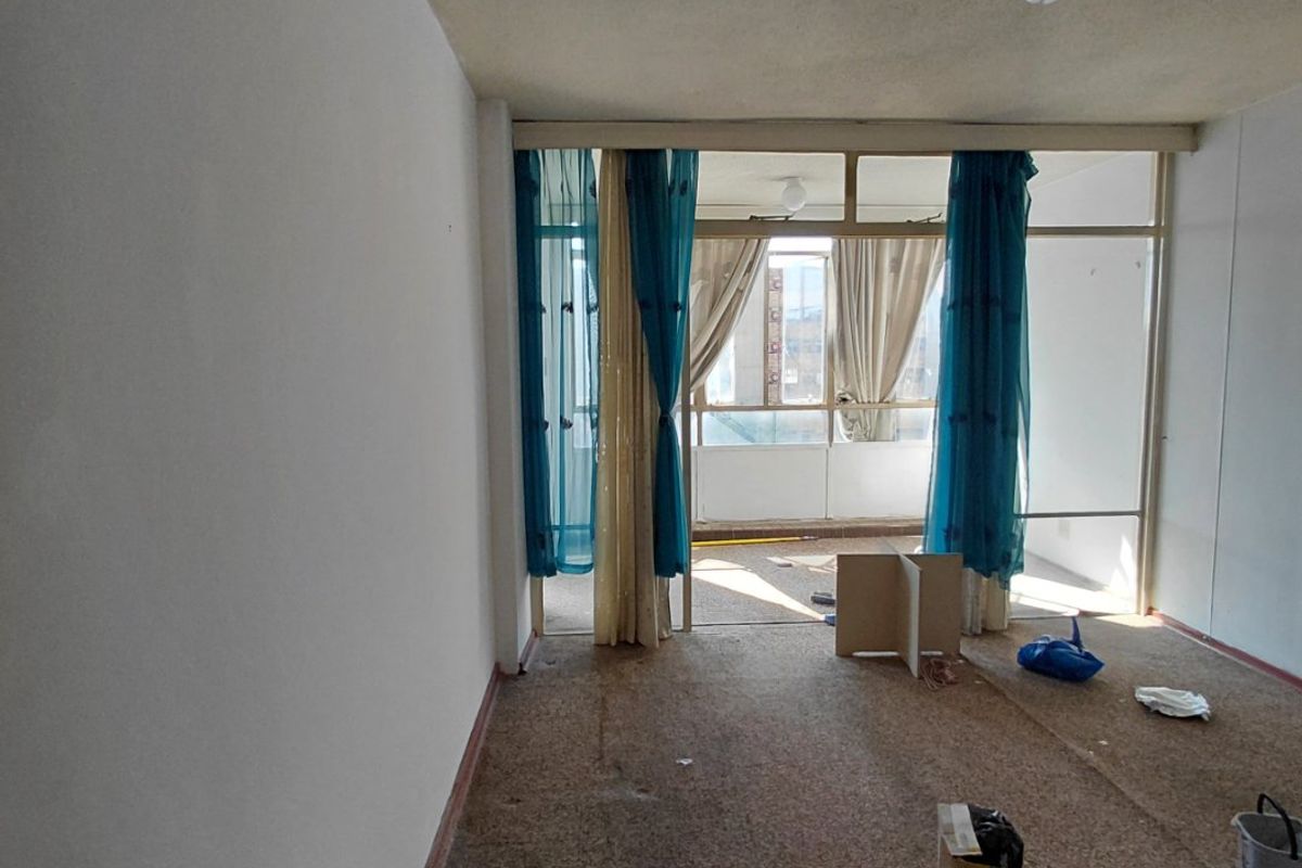 An empty living room featuring large glass sliding doors leading to a balcony, with carpet flooring and a ceiling light fixture.