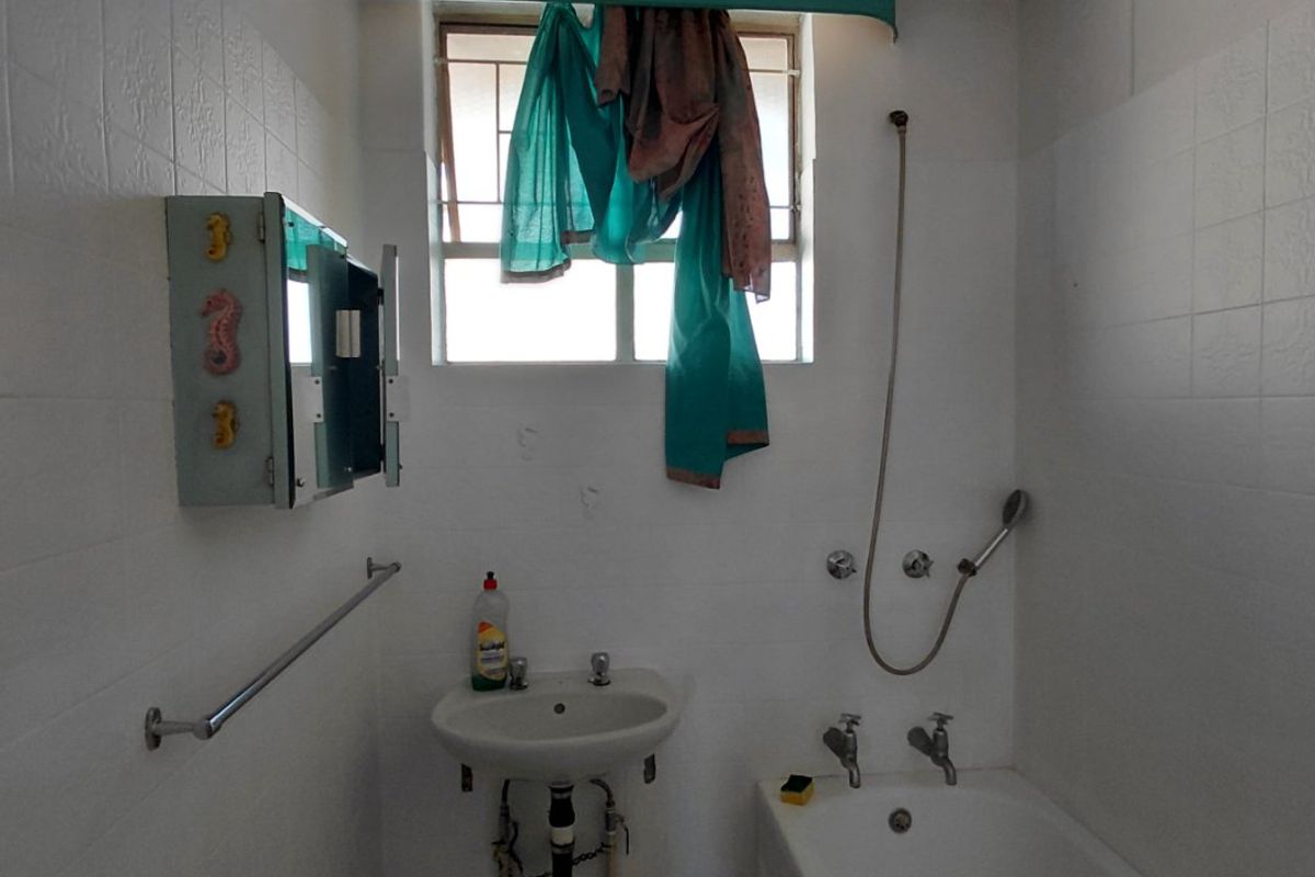 A dated bathroom featuring a wall-mounted basin, bathtub with shower mixer, and tiled finishes, requiring modernization and cosmetic updates.