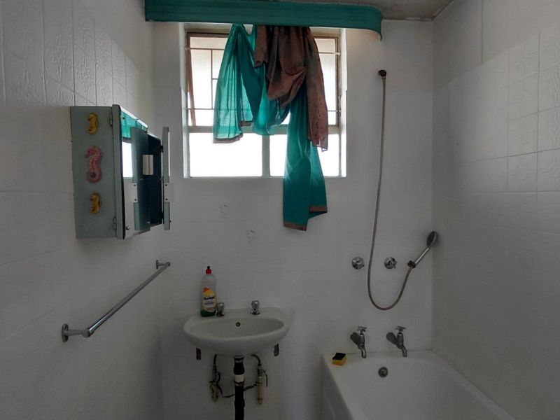 A dated bathroom featuring a wall-mounted basin, bathtub with shower mixer, and tiled finishes, requiring modernization and cosmetic updates.