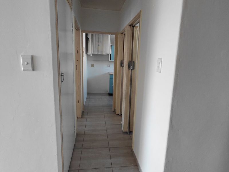 A narrow apartment hallway featuring tiled flooring and built-in storage, leading towards the kitchen area. The space requires minor finishing and cosmetic updates.