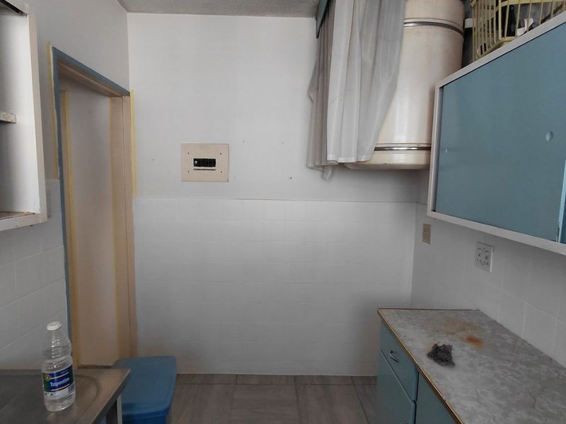 A functional laundry area featuring built-in cabinetry, tiled splashbacks, and an electric water heater, offering potential for modernization and improved utility space.
