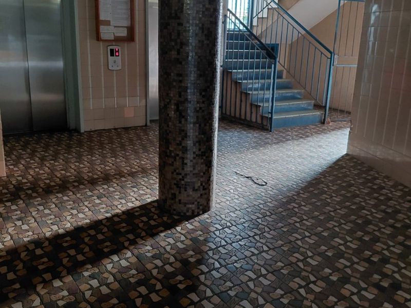 A communal apartment building entrance lobby featuring a mosaic tiled central column, elevator access, and a staircase with metal handrails.