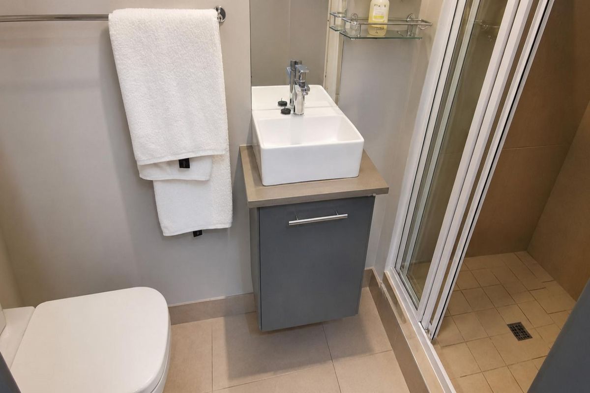 Modern bathroom featuring a wall-mounted vanity with a vessel sink, chrome fixtures, and a glass-enclosed shower with tiled flooring.