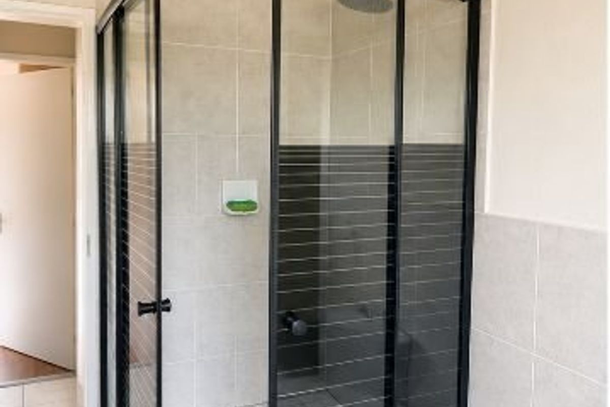 A modern bathroom featuring a corner shower enclosure with black framing, a rain shower head, and neutral wall tiling.