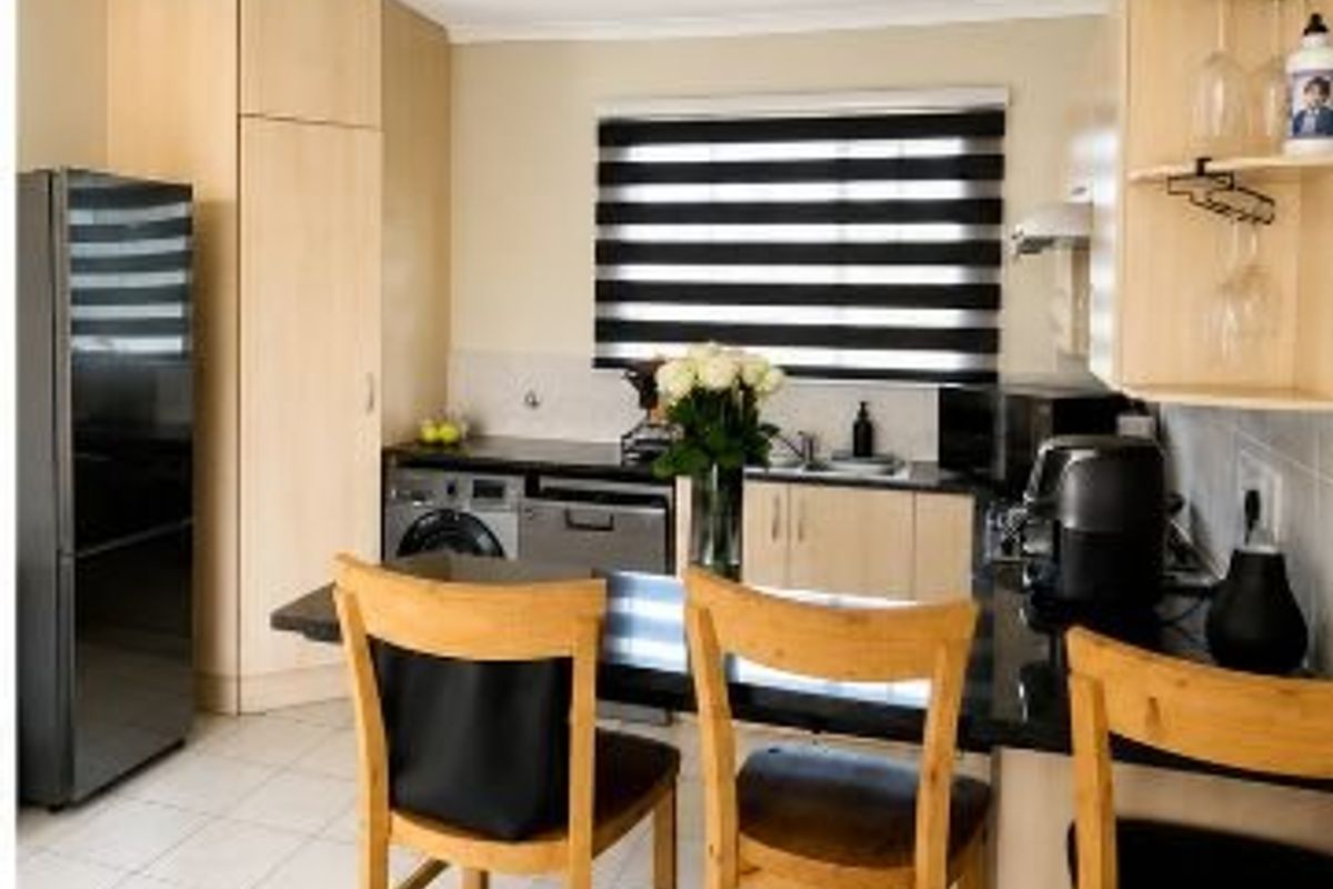 A functional kitchen featuring light wood cabinetry, dark granite countertops, tiled flooring, and a breakfast bar area with modern window blinds.