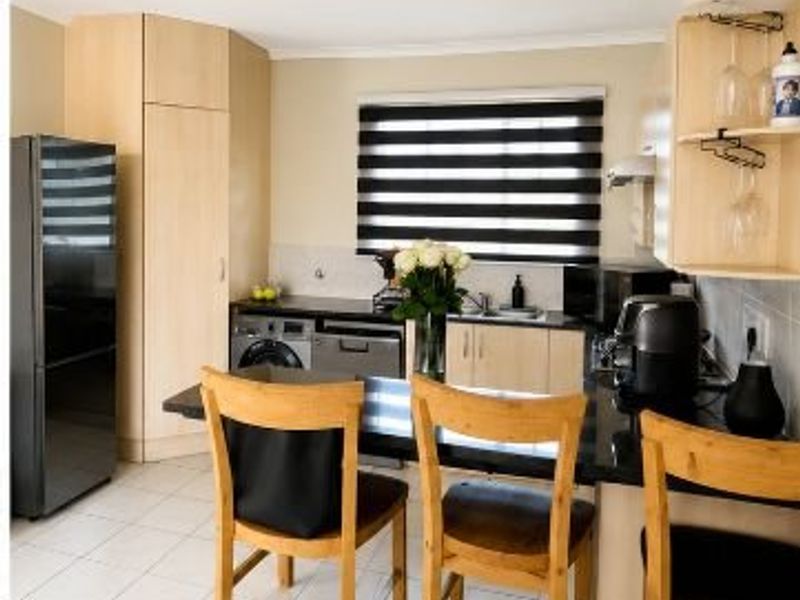 A functional kitchen featuring light wood cabinetry, dark granite countertops, tiled flooring, and a breakfast bar area with modern window blinds.