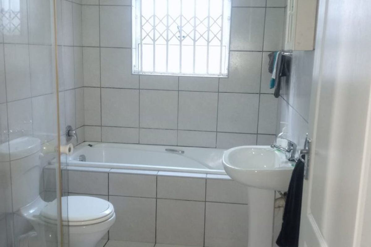 A functional bathroom featuring a bathtub, pedestal basin, toilet, and a separate shower enclosure with white tiled finishes throughout.