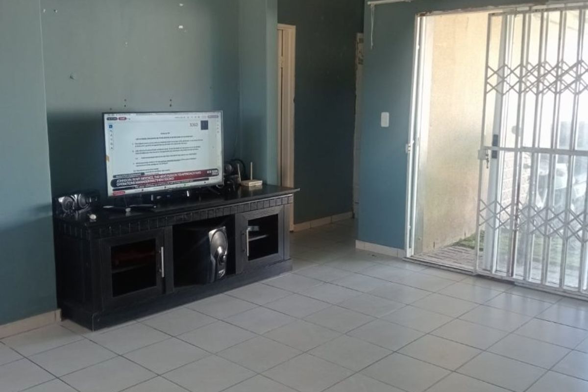 A living room featuring tiled flooring, recessed lighting, and a sliding glass door with a security gate leading to the exterior.