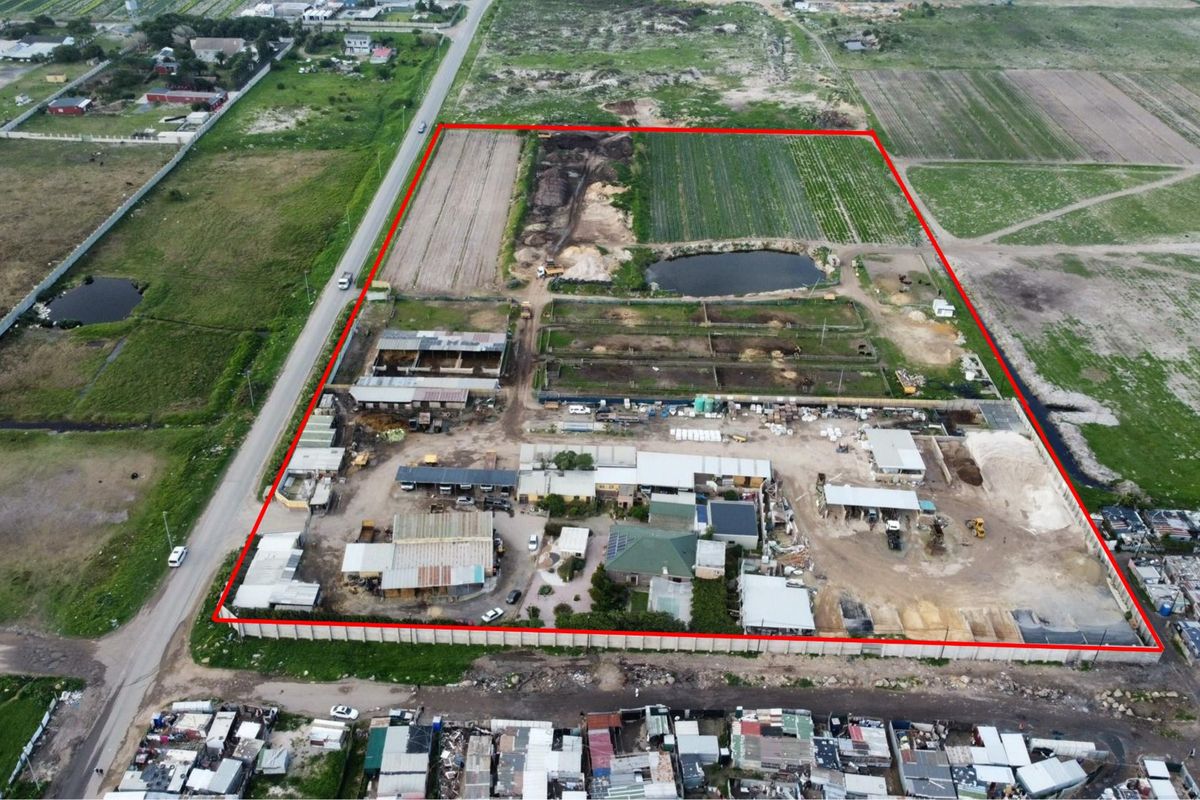 Aerial view of a large farm property featuring multiple outbuildings, storage areas, a water reservoir, and extensive cultivated land within a fenced perimeter.