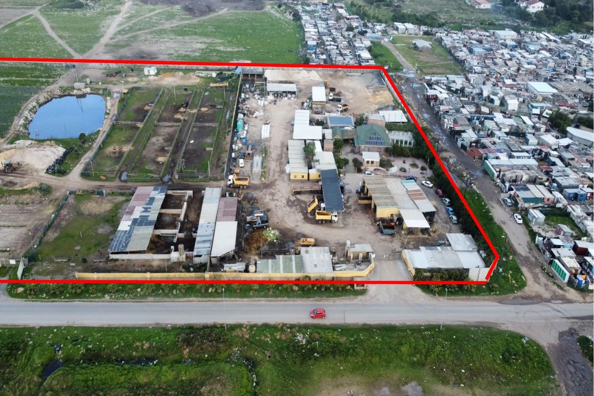 Aerial view of a farm property featuring multiple outbuildings, storage sheds, a water reservoir, and perimeter fencing, situated adjacent to a residential area.