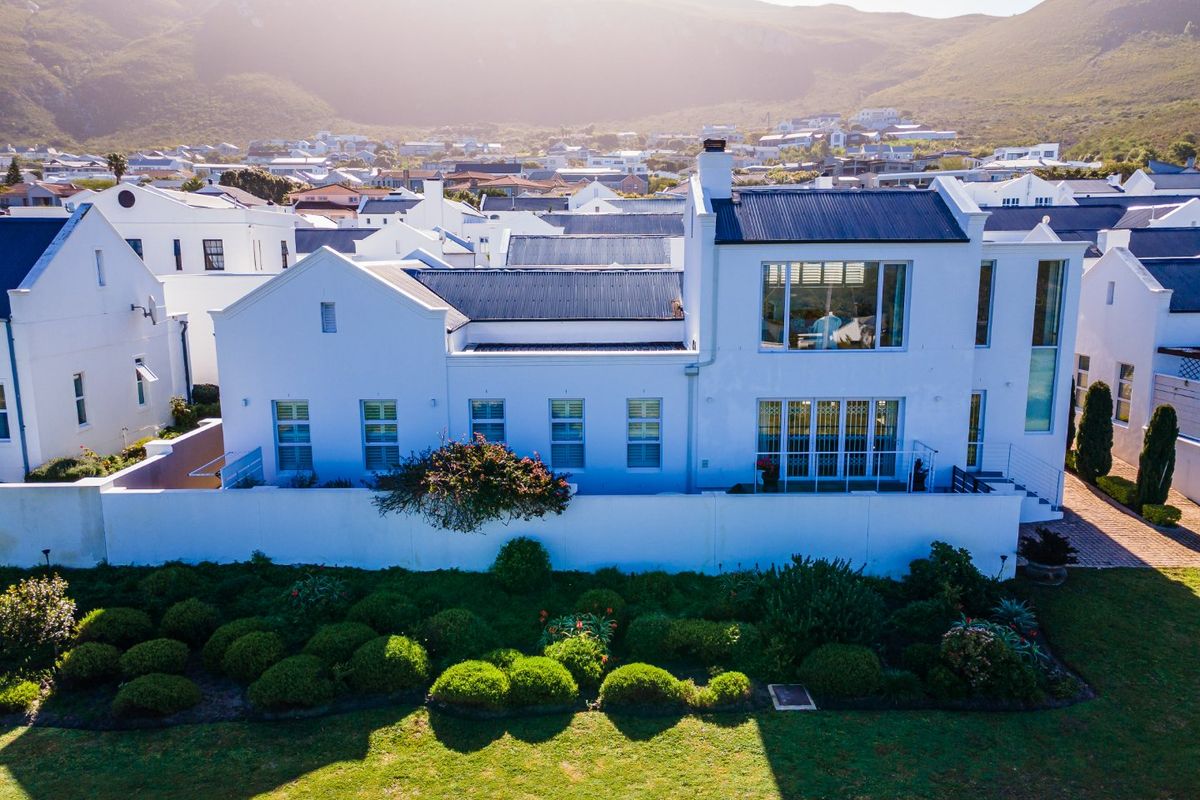 Aerial view of a modern white residential property featuring a corrugated metal roof, landscaped garden, and expansive windows set against a mountain backdrop.