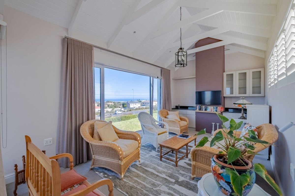 Bright living room featuring a vaulted ceiling with exposed beams, built-in cabinetry, and large sliding doors offering expansive coastal views.