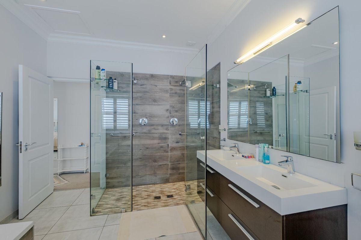 Modern bathroom featuring a spacious walk-in shower with wood-look tiling, a double vanity with integrated sinks, and a large wall-mounted mirror.