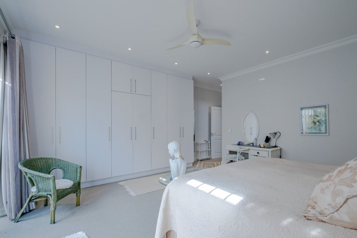 Spacious bedroom featuring extensive floor-to-ceiling built-in cupboards, neutral carpeting, and a modern ceiling fan with recessed lighting.