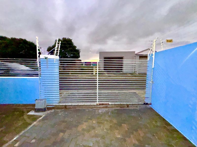 Front entrance view featuring a secure metal gate, electric fencing, and a paved driveway leading to the property.