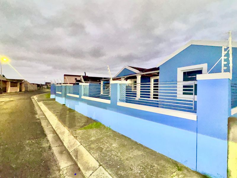 Front exterior view of a blue house featuring a perimeter wall with integrated electric fencing and metal slat security panels.