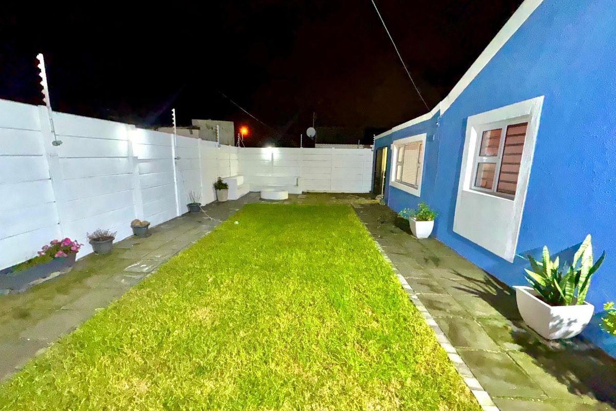 A rear garden area featuring a central lawn, paved pathways, and perimeter precast concrete walling with integrated electric fencing.