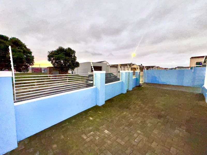 A paved front driveway area enclosed by a blue boundary wall with integrated electric fencing.
