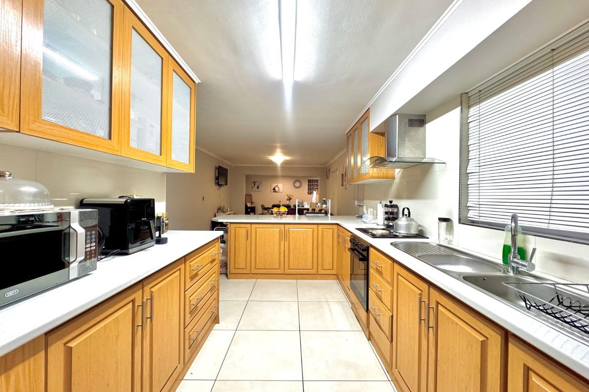 A functional kitchen featuring wooden cabinetry, laminate countertops, a built-in oven, and an extractor fan, with tiled flooring throughout.