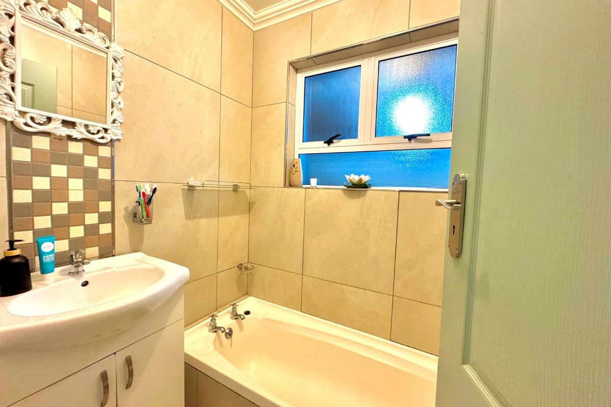 A well-maintained bathroom featuring a vanity cabinet, bathtub, and neutral wall tiling with a decorative mosaic accent strip.
