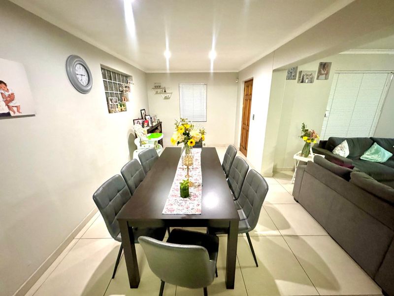 An open-plan dining and living area featuring neutral tiled flooring, recessed downlighting, and a glass block feature window.