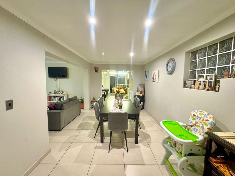 A bright dining area featuring large format floor tiles, recessed downlighting, and a glass block window, flowing into an adjacent living space.