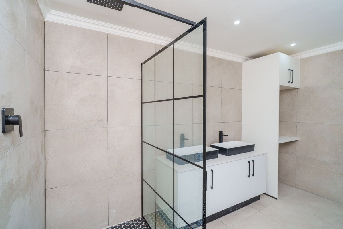 Modern bathroom featuring a double vanity with black fixtures, a sleek black-framed glass shower screen, and contemporary neutral tiling.