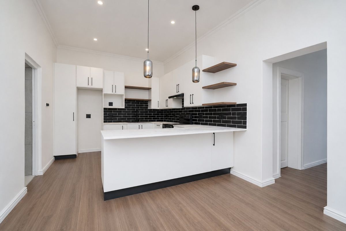 Modern kitchen featuring white cabinetry, black subway tile backsplash, stone countertops, and a functional island with integrated lighting and wood-look laminate flooring.