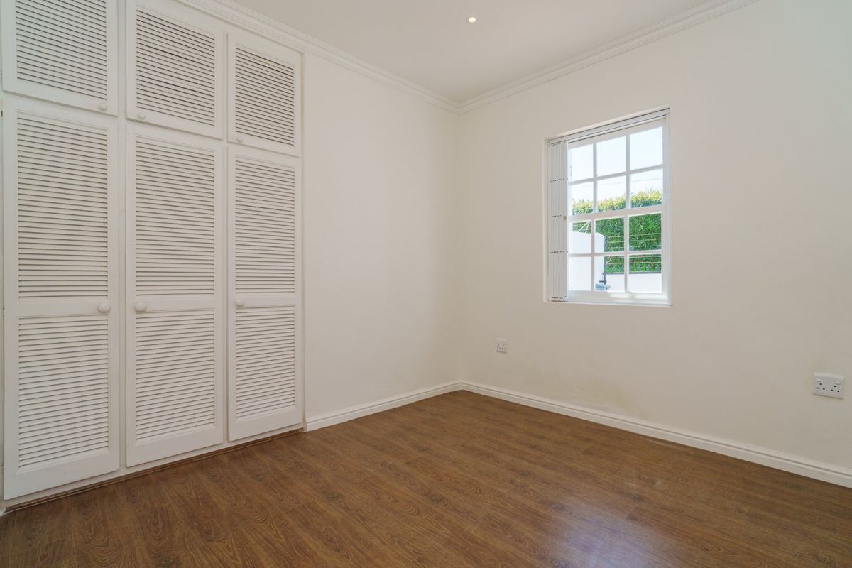 A bright, empty bedroom featuring laminate flooring, built-in louvered cupboards, and a classic grid window with natural light.