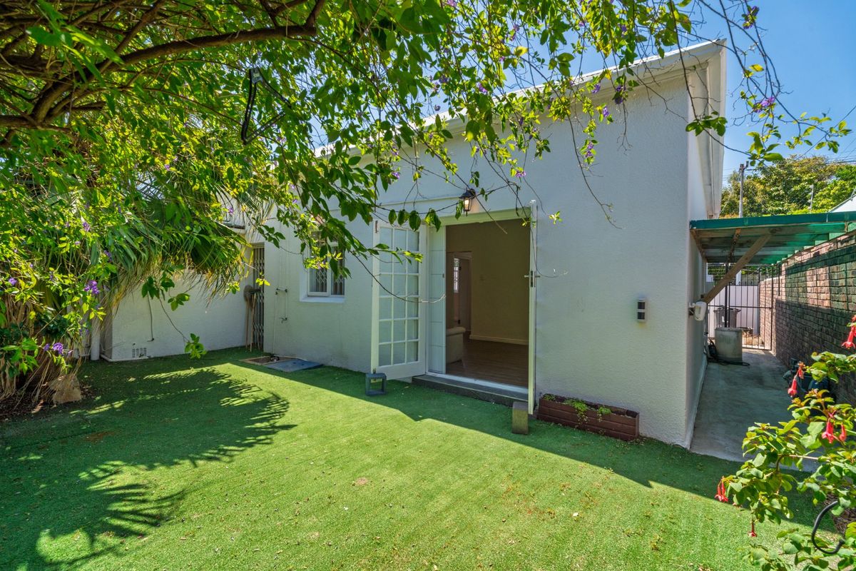 A view of the rear exterior featuring a white facade, french doors leading inside, and a well-maintained artificial lawn area.
