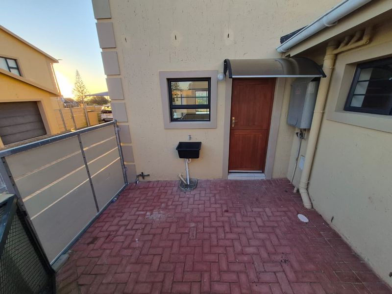 A paved rear courtyard area featuring an external utility sink, a timber door, and an overhead awning attached to the townhouse exterior.