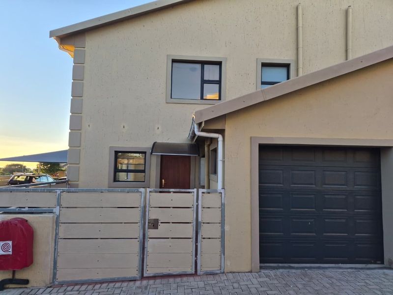Front elevation of a townhouse featuring a single garage, paved driveway, and secure gated entrance with modern aluminium window frames.