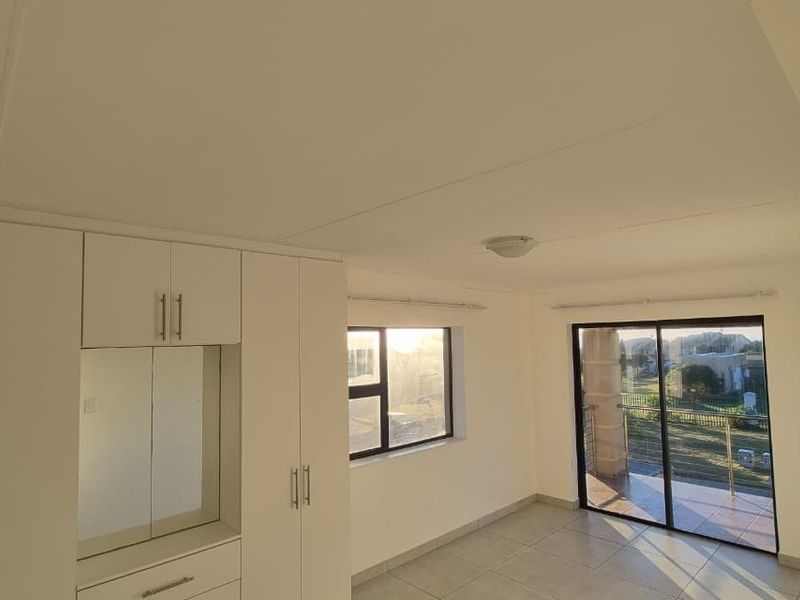 A bright, empty bedroom featuring built-in cupboards, tiled flooring, and a sliding glass door leading to an outdoor balcony area.